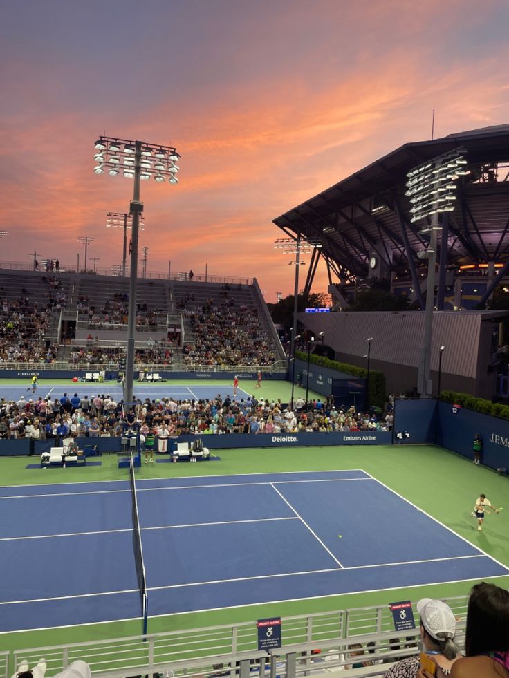 a tennis match is being played on a blue and green court as the sun sets