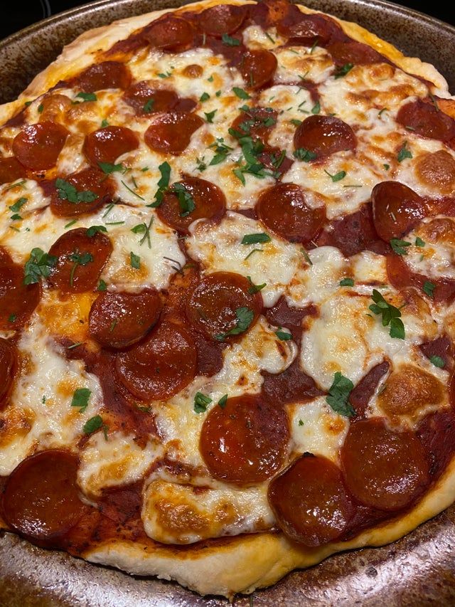 a pepperoni pizza with cheese and herbs on it sitting in a metal pan, ready to be eaten