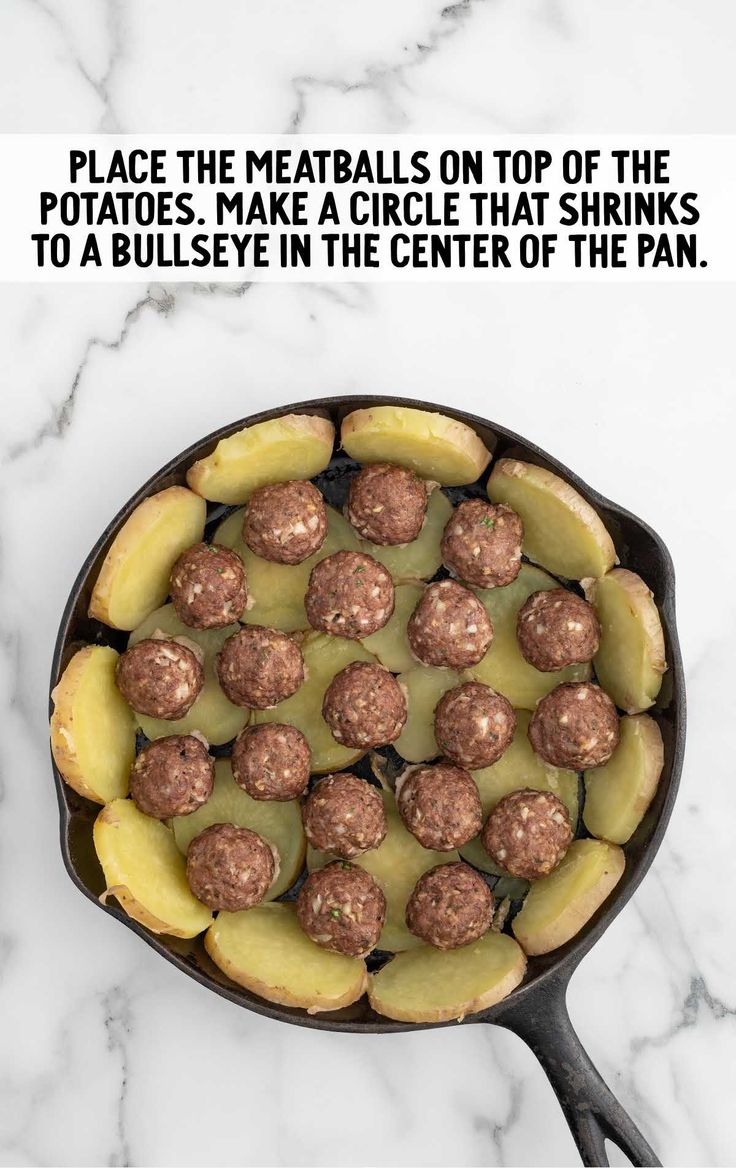 a skillet filled with meatballs and potatoes on top of a white marble counter