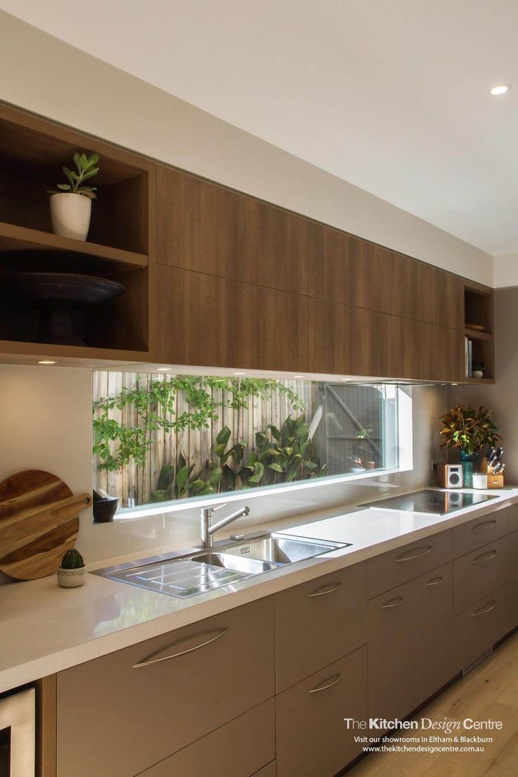 a kitchen with wooden cabinets and white counter tops, plants on the window sill