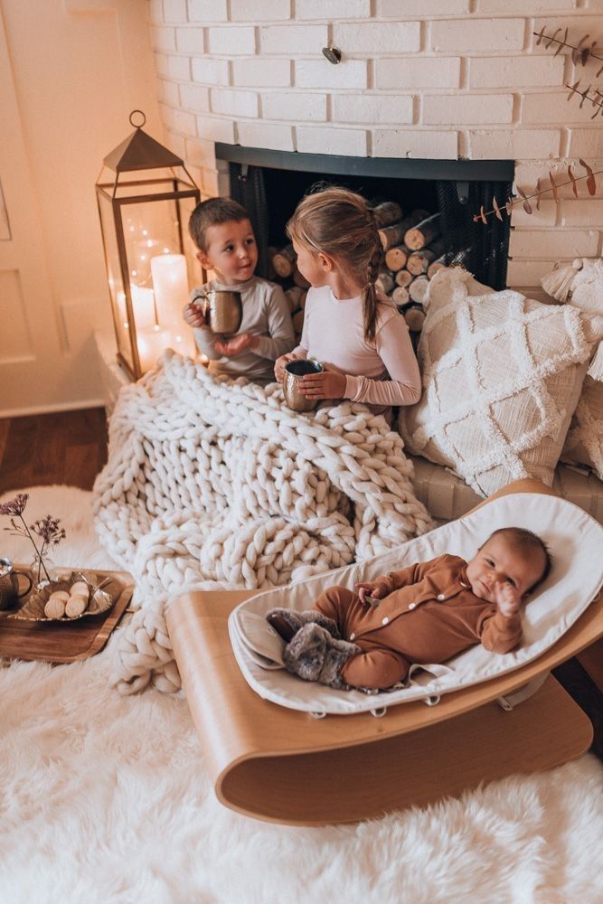 two children sitting in a baby bassinet next to a fire place with candles