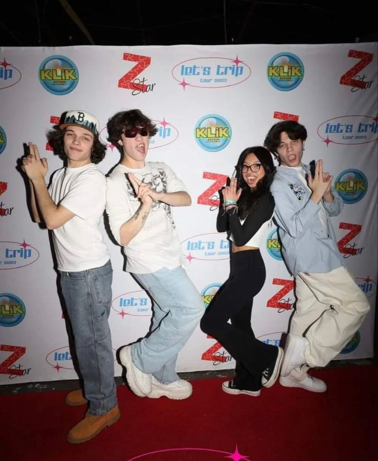 four people posing for a photo in front of a red carpeted wall with the z logo on it