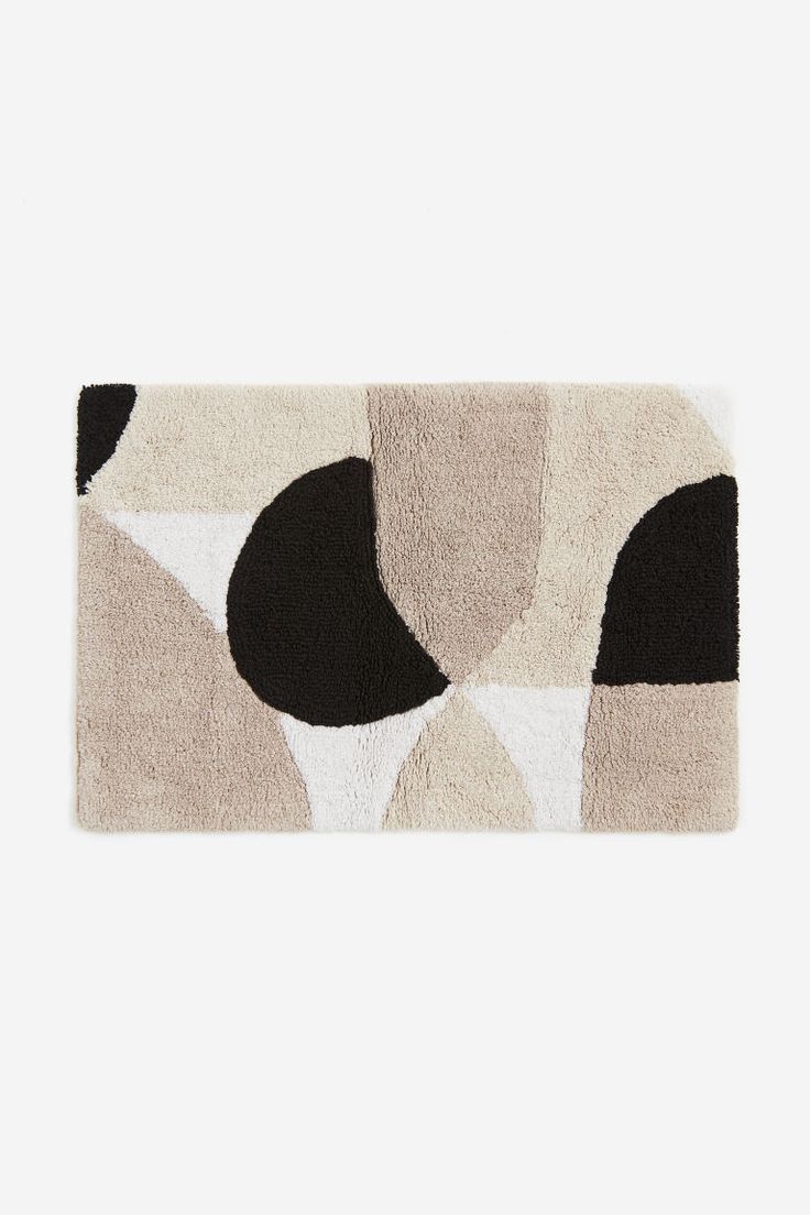 a rug with black, white and beige shapes on the floor in front of a gray wall