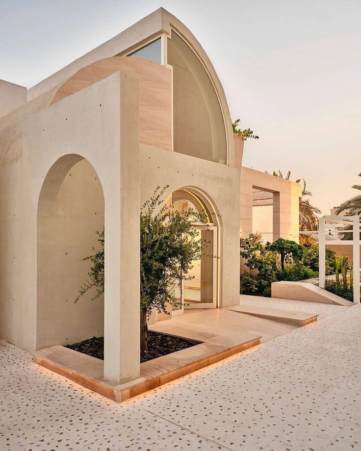 a white building with a tree in the center and an archway leading to it on one side