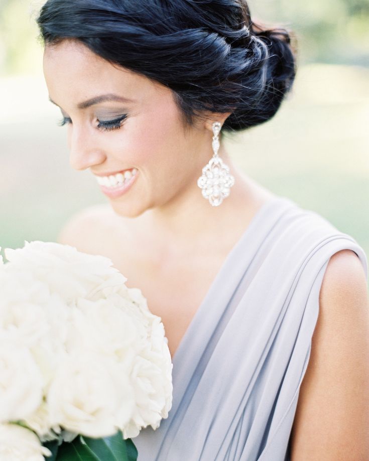 a woman in a gray dress holding a white bouquet and smiling at the camera with her eyes closed