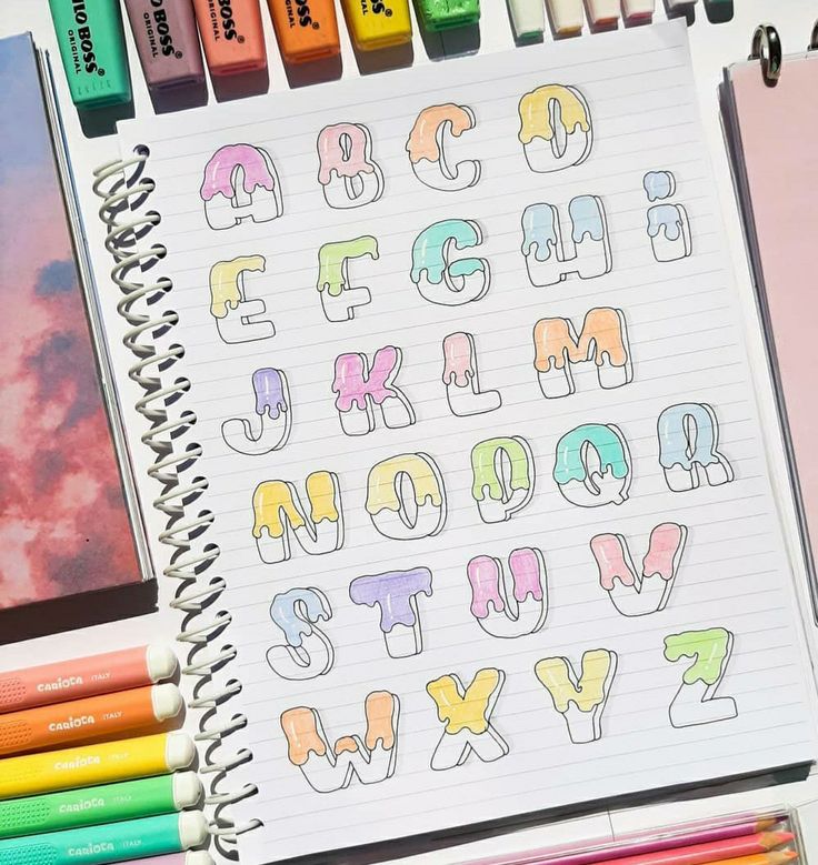 an open notebook with letters and numbers drawn on it next to colored crayons