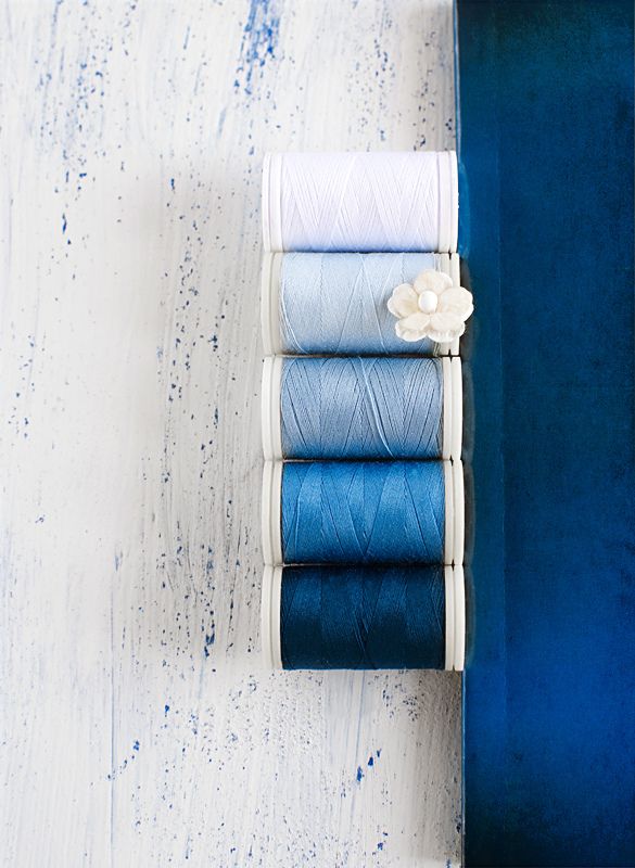 four different colored spools of thread in a blue box on a white wooden surface