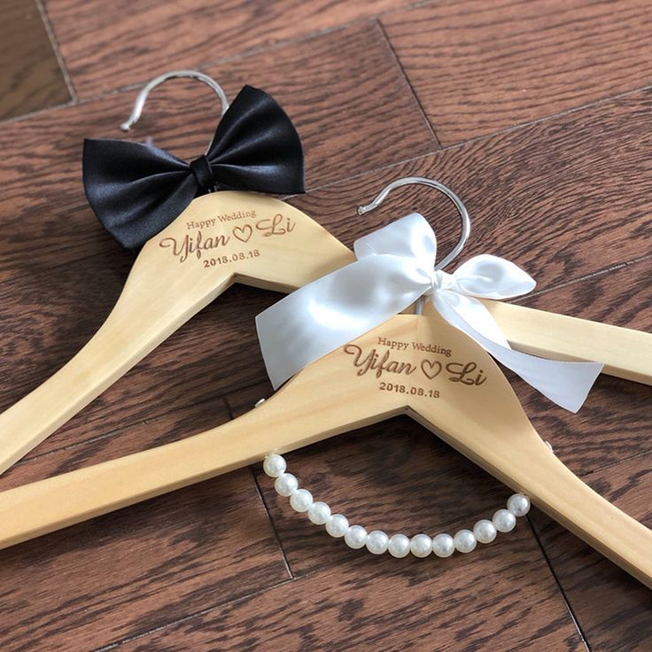 two personalized wooden hangers with white pearls and black bows