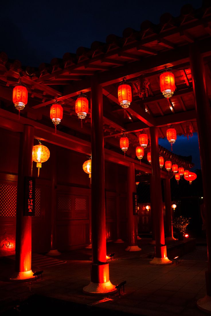 lanterns lit up in the night sky above an outdoor area with columns and pillars covered in red lights