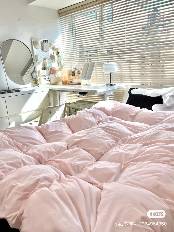 an unmade bed with pink sheets and pillows in a bedroom next to a desk