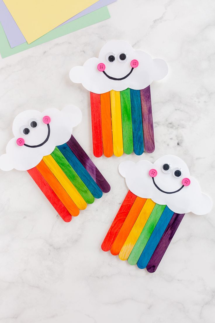 three pops sticks with rainbows and clouds painted on them sitting on a marble surface