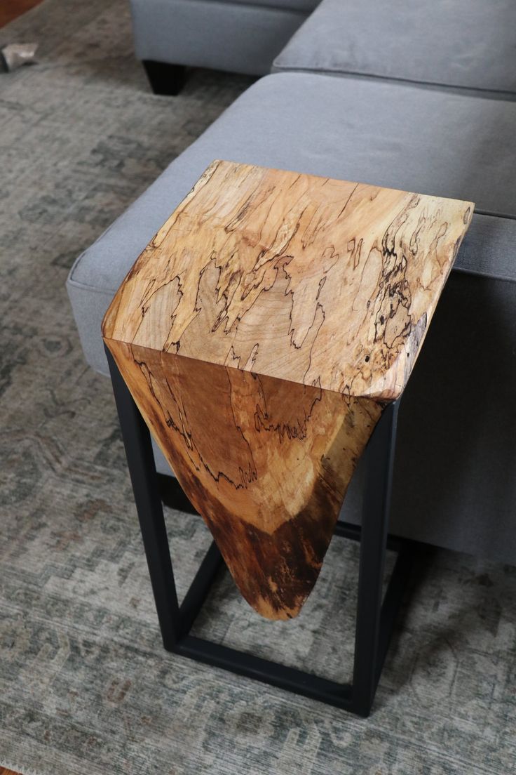 a wooden table sitting on top of a metal stand in front of a gray couch