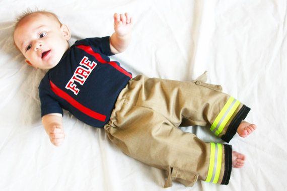 a baby boy laying on top of a bed wearing a fireman shirt and pants