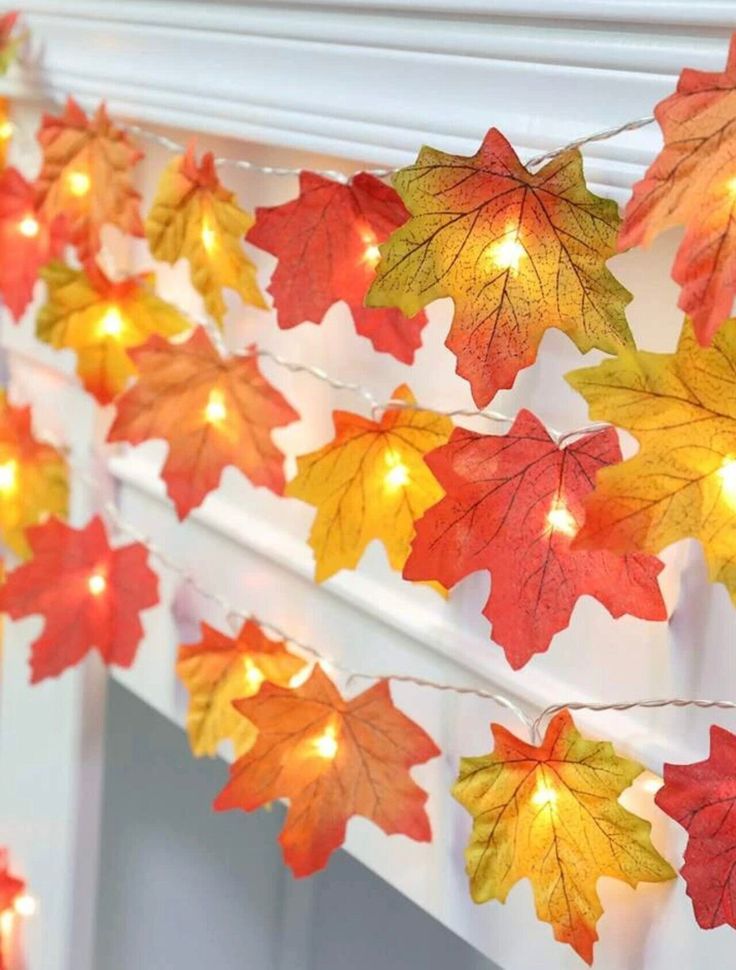 fall leaves are hanging from a mantle with lights on it and some candles in the background