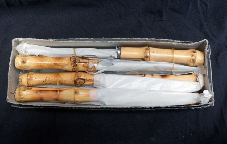 three wooden dolls are in a box on a black cloth covered tablecloth, one is wrapped in white paper and the other is made from bamboo