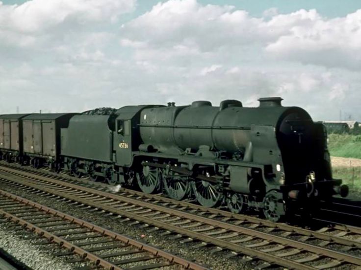 a black train traveling down tracks next to a lush green field on a cloudy day