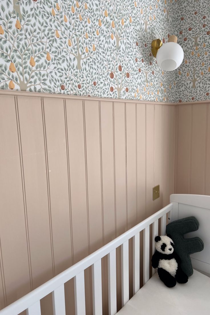 a stuffed panda bear sitting on top of a crib next to a wallpaper