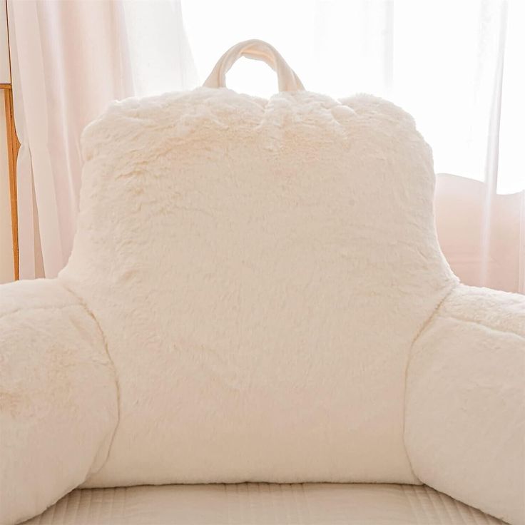 a white teddy bear shaped pillow sitting on top of a bed next to a window