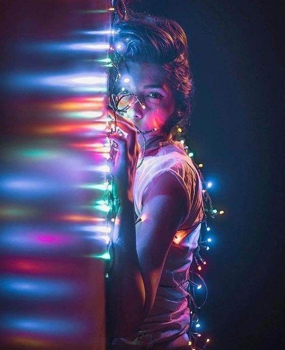 a woman standing next to a wall covered in christmas lights