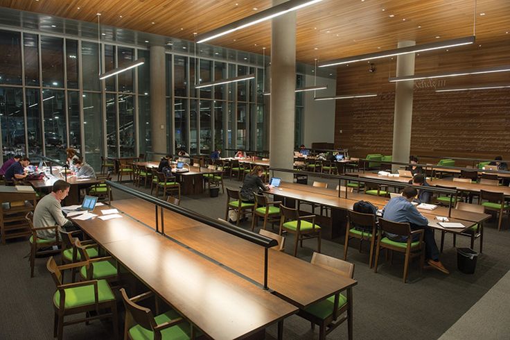 people sitting at desks in an open area with large windows and wood paneling