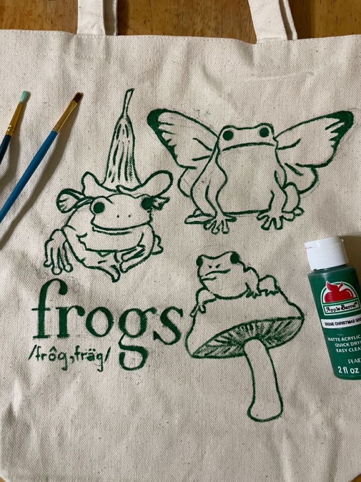 a tote bag sitting on top of a wooden table next to paint and pencils