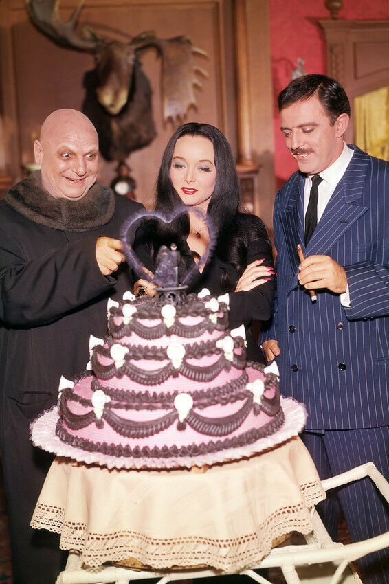 two men and a woman standing next to a cake