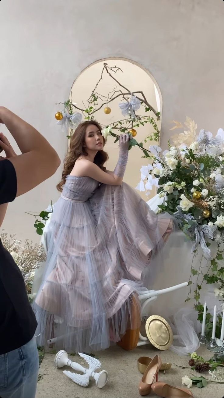 a woman in a dress is sitting on a chair with flowers and shoes around her