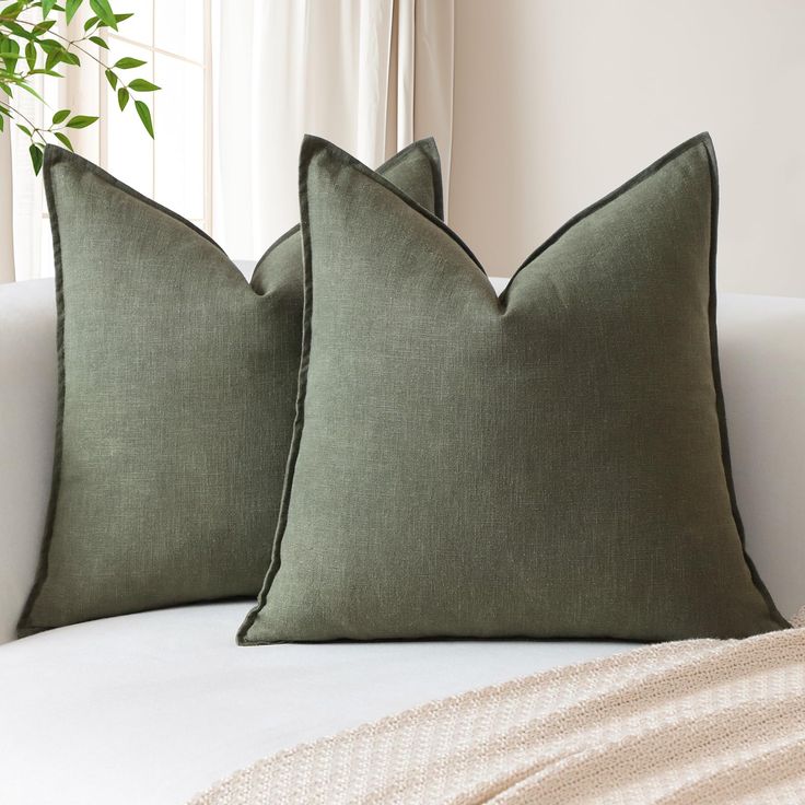 two green pillows sitting on top of a white couch next to a potted plant