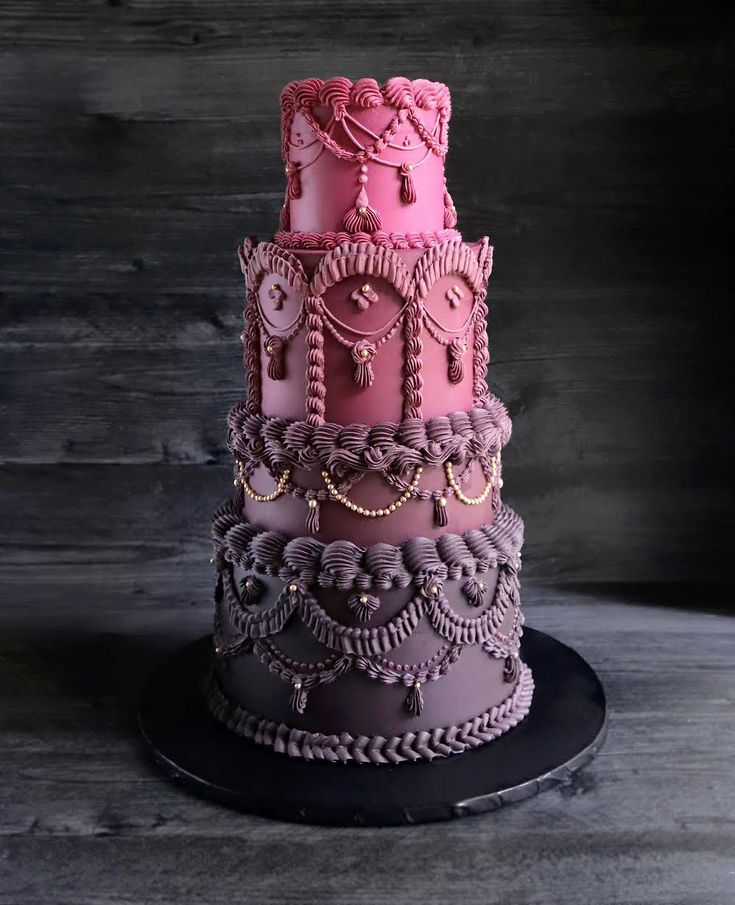 a three tiered pink and purple cake on a black platter with chains around it