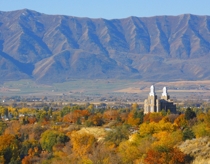 an old church in the middle of autumn with mountains in the background and trees turning colors