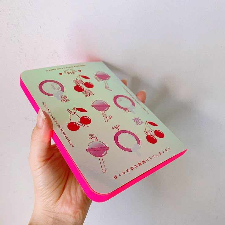 a person holding up a pink and green notebook with stickers on the front cover