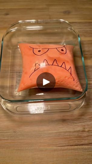 an orange pillow sitting on top of a wooden table next to a glass container with a face drawn on it