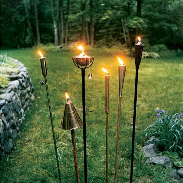 four candles are lit in the grass near a stone wall