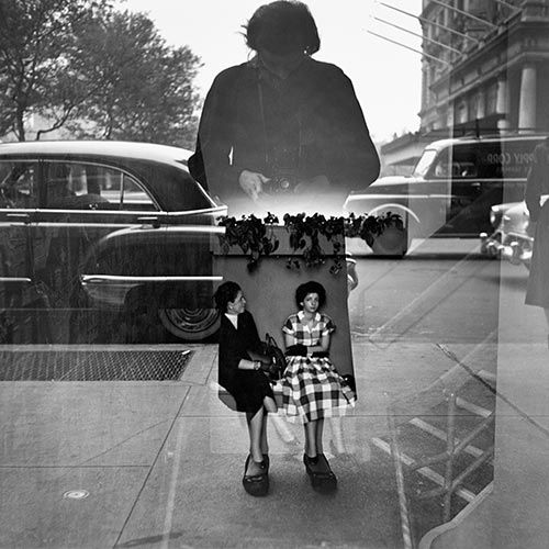 two women sitting on a bench in front of a window with an image of a woman standing behind them