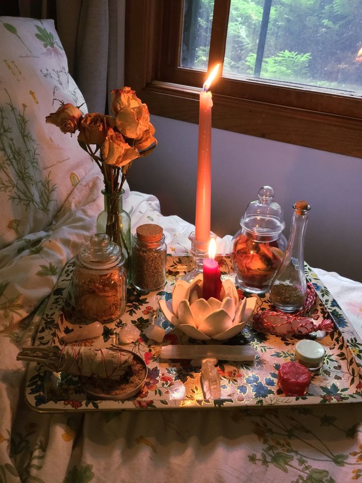 a candle is lit on a tray with flowers and other items around it in front of a window