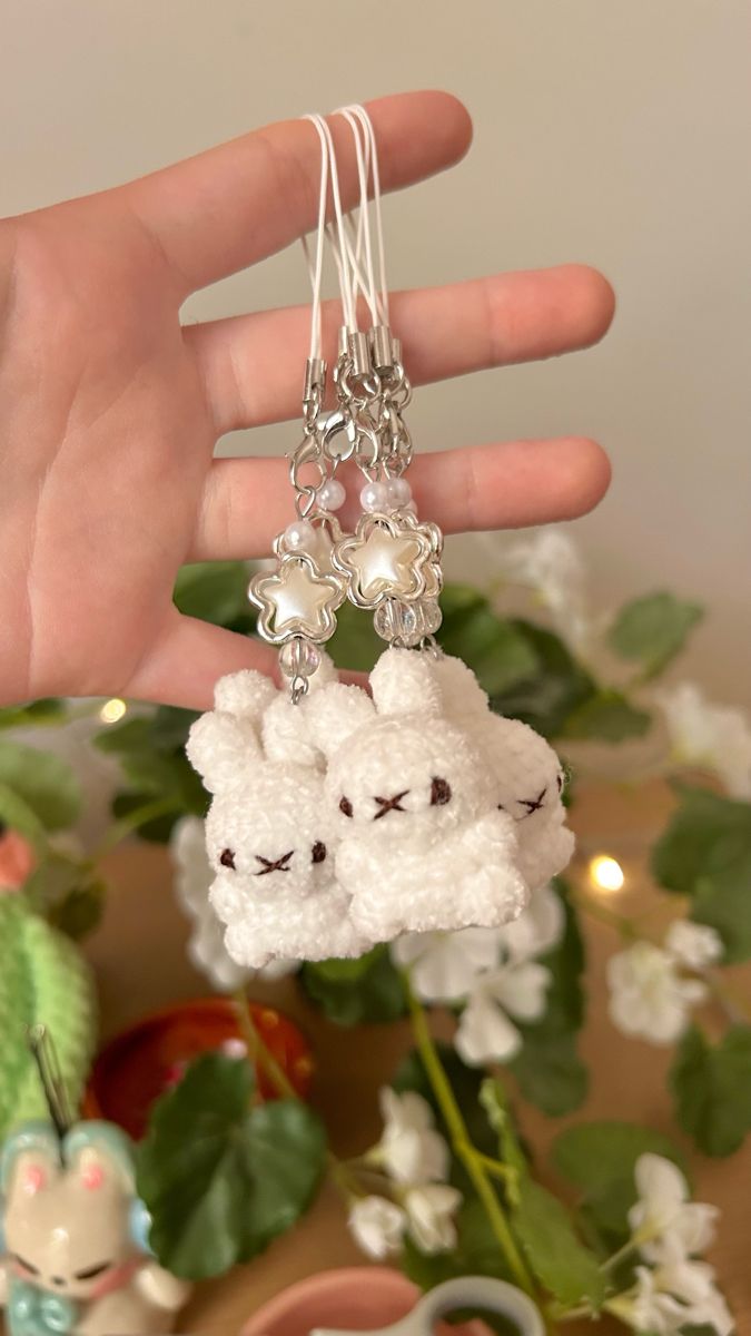 a hand is holding two sheep keychains with pearls on each end and beads hanging from the ends