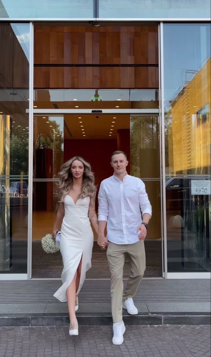 a man and woman holding hands walking out of a building with glass doors on both sides