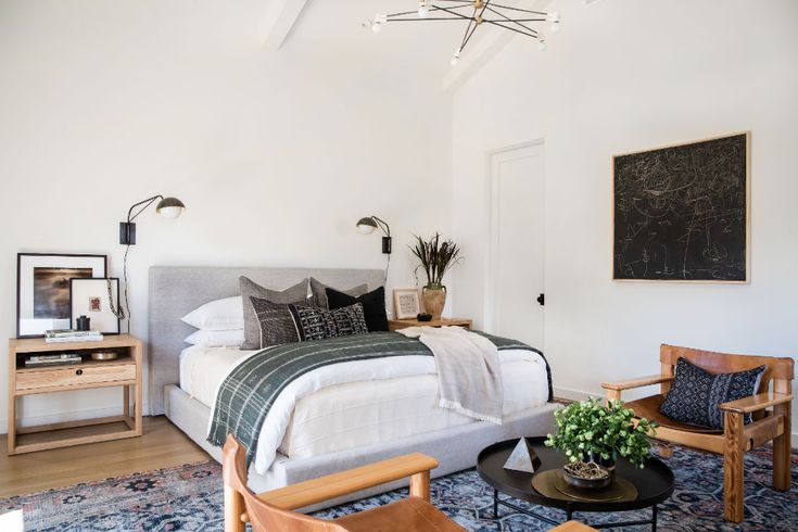 a bedroom with a large bed and wooden chairs in front of the bed is decorated with plants