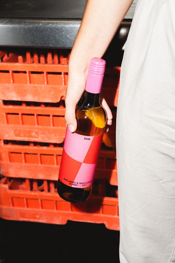 a person holding a bottle of wine in front of some oranges and red crates