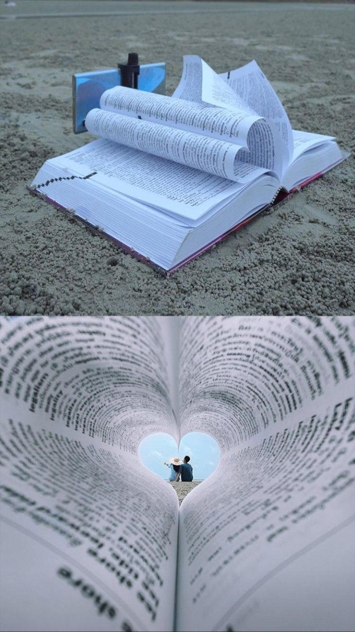 an open book laying on top of a sandy beach next to a heart shaped hole