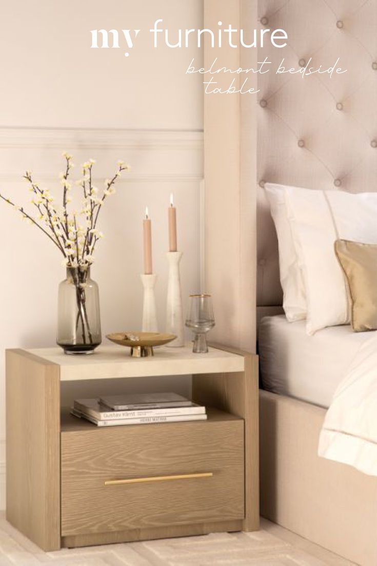 a nightstand with flowers and candles on it next to a bed