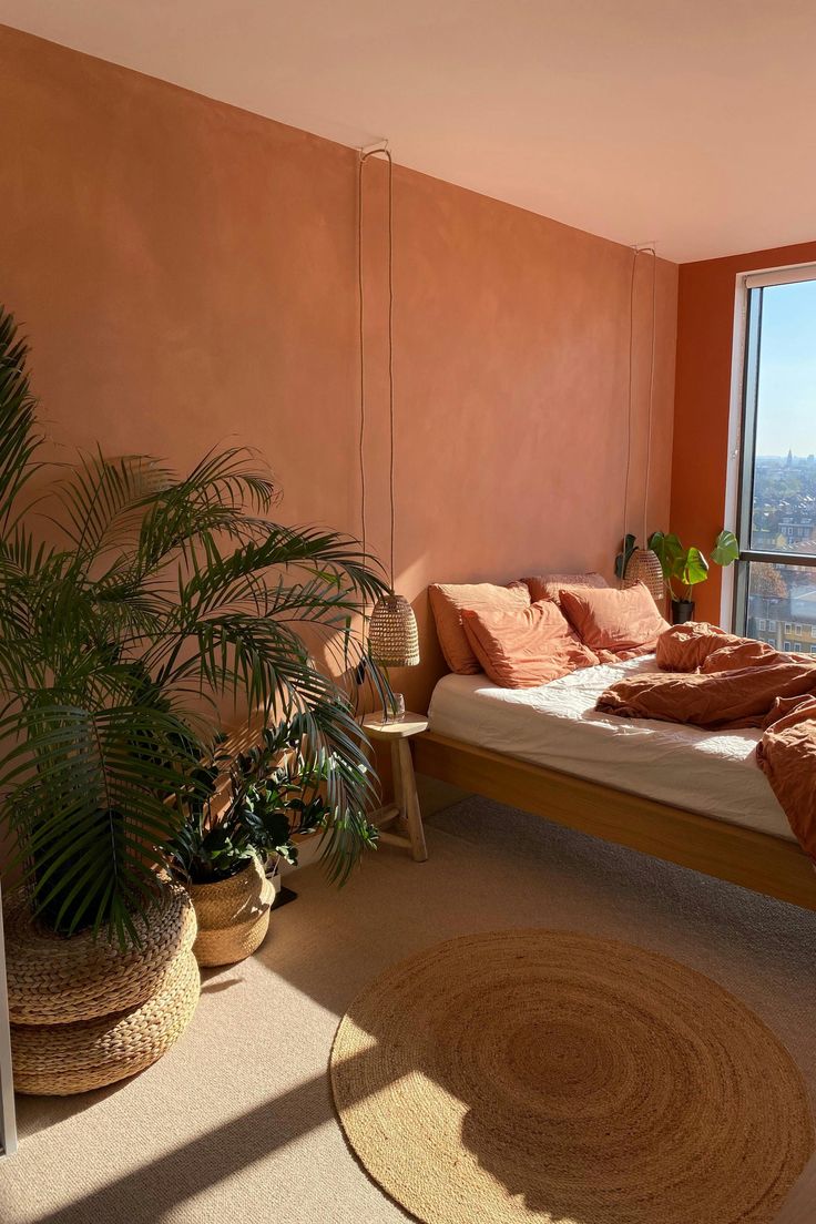 a bedroom with a bed, plant and large window overlooking the cityscape outside