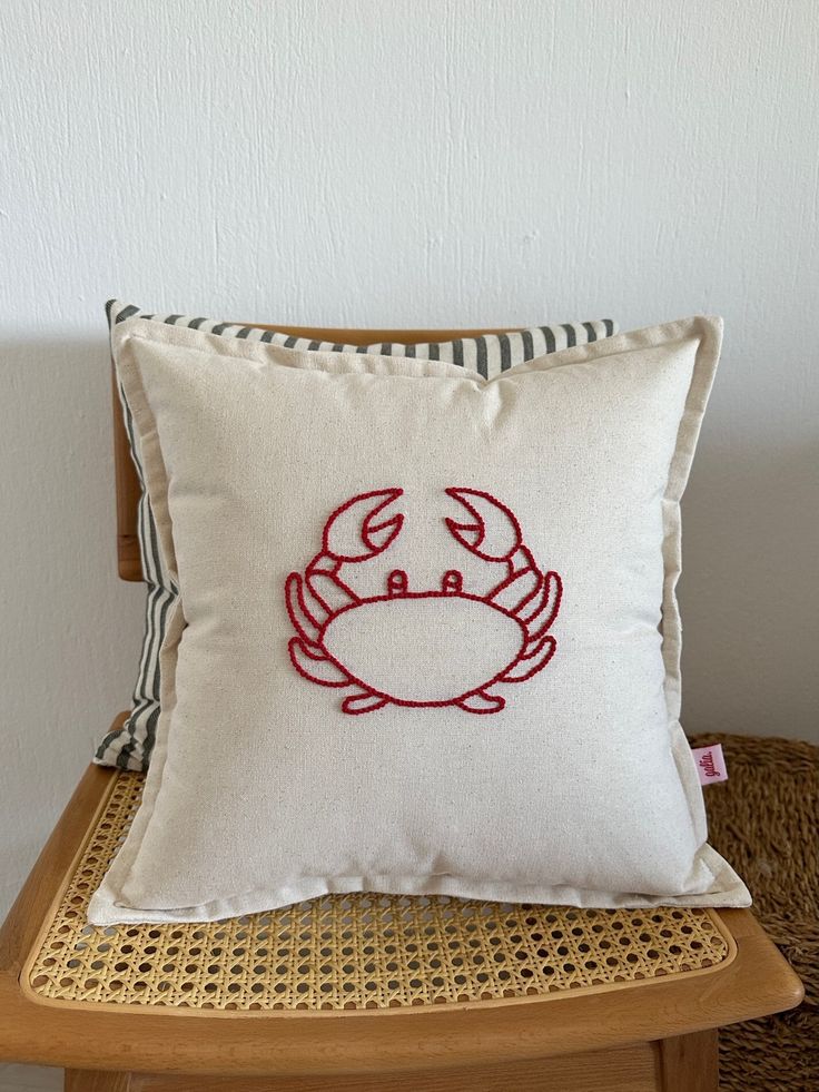 a pillow with a crab embroidered on it sitting on a chair in front of a white wall