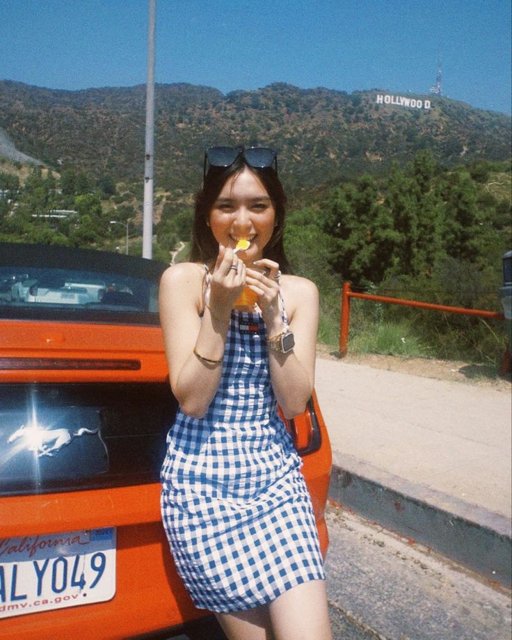 a woman sitting on the hood of an orange car eating something out of her mouth