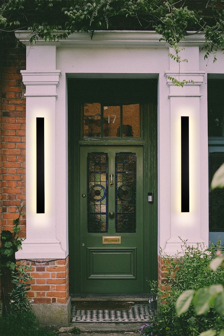 a green front door with two lights on it's sides and some plants in the foreground