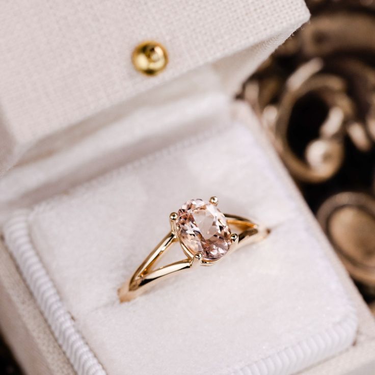 an engagement ring in a white box with gold accents and a pink diamond on the side