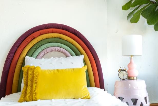 a bed topped with pillows next to a lamp and a rainbow wall hanging above it