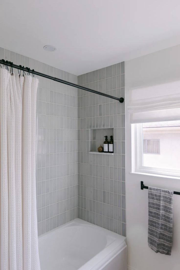 a white bath tub sitting under a window next to a shower curtain in a bathroom