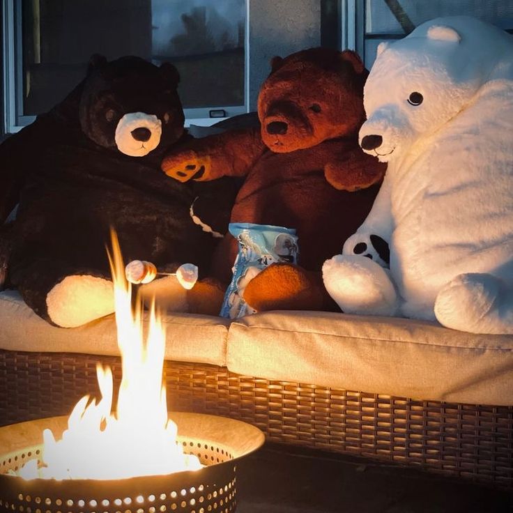 three teddy bears sitting on a couch next to a fire pit with their lights on