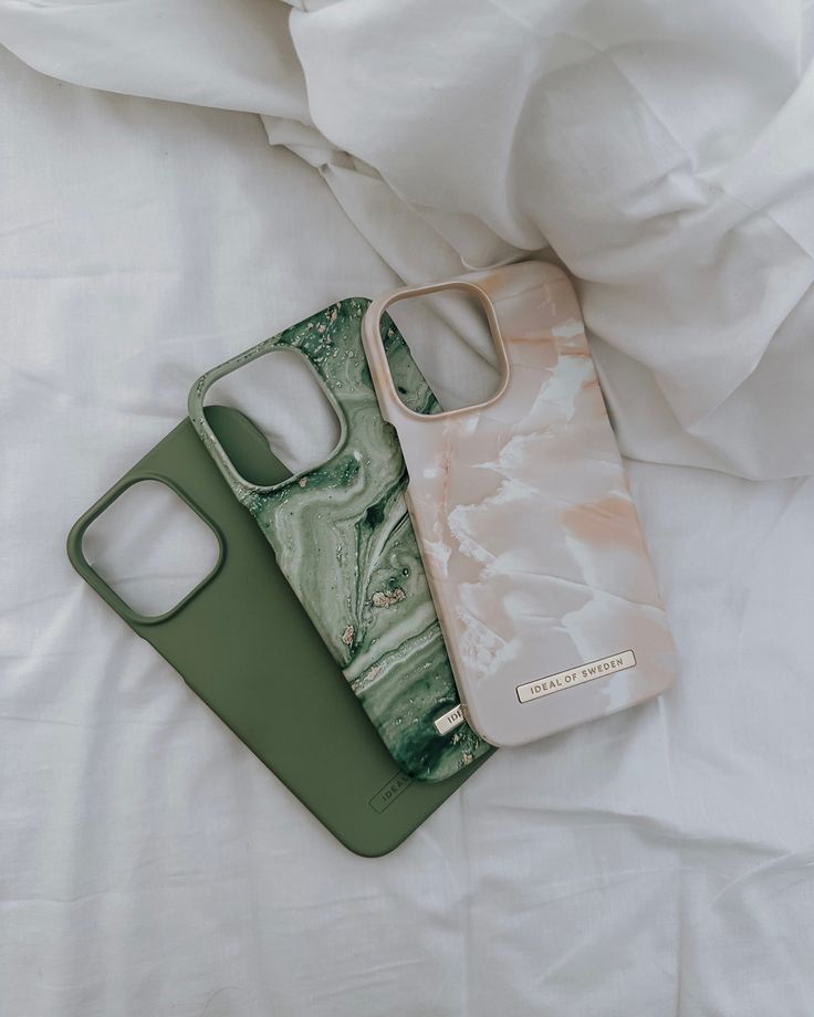 two cell phones sitting on top of each other next to a white bed with sheets